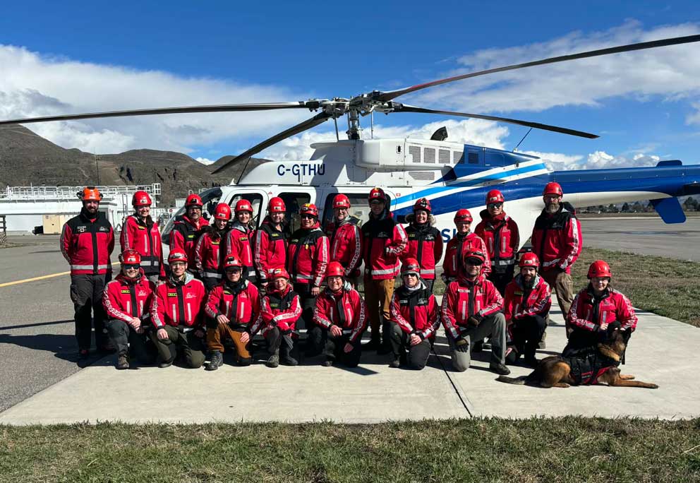 Kamloops Search and Rescue volunteers in red rescue gear posing with helicopter and search dog during training exercise