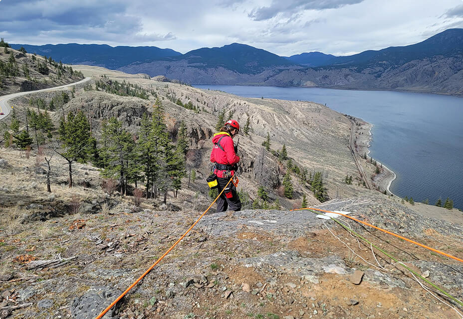 Kamloops Search and Rescue member performing rope rescue training on cliff above Kamloops Lake with rugged mountain landscape